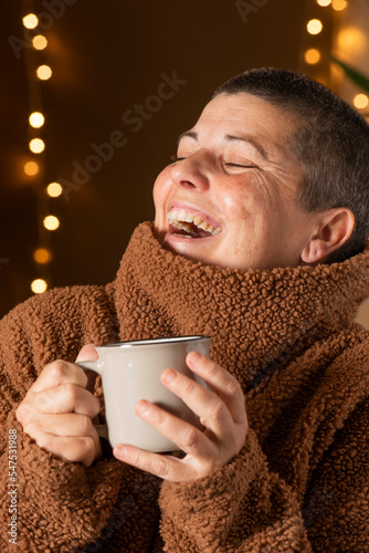 Woman with winter jumper and coffee cup, out-of-focus city or celebration lights behind.
