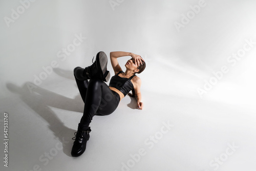 Stylish young woman in a black hat and jacket, sitting in a spectacular pose on a white background in a photo studio