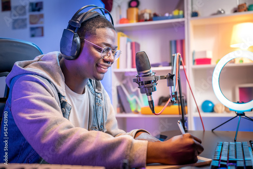 Young smiling man wearing headphones and talking into a microphone at the radio station recording podcast. Music production concept.