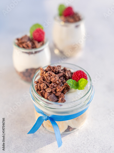 Domowe, zdrowe śniadanie. Naturalny grecki jogurt z czekoladowym musli, bananami i malinami.