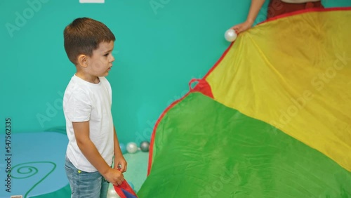 Caucasian little boy standing and holding a piece of colorful material with his teacher, games in kindergarten. High quality 4k footage photo