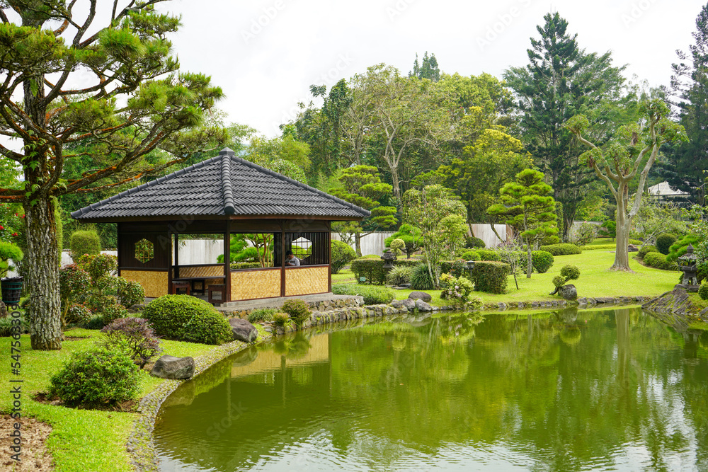 Traditional oriental park or garden from Japan or China with fish pond, lake or river, wooden bridge, meadow, and trees. Japanese garden design. Taman Bunga Nusantara, Cianjur, West Java, Indonesia.