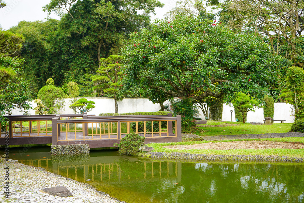 Traditional oriental park or garden from Japan or China with fish pond, lake or river, wooden bridge, meadow, and trees. Japanese garden design. Taman Bunga Nusantara, Cianjur, West Java, Indonesia. Traditional oriental park or garden from Japan or China with fish pond, lake or river, wooden bridge, meadow, and trees. Japanese garden design. Taman Bunga Nusantara, Cianjur, West Java, Indonesia.