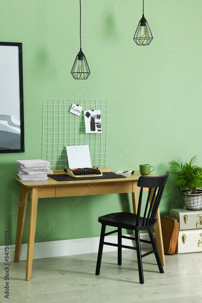 Fototapeta premium Typewriter, stack of papers and mood board on wooden table near pale green wall. Writer's workplace