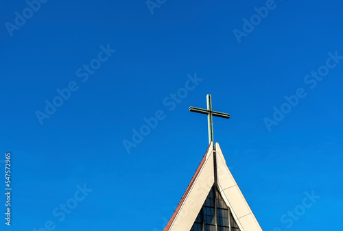 Big cross on the roof of Roman catholic church. Church steeple with blue sky. 