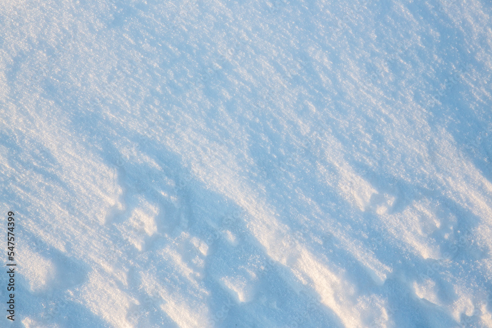 Fototapeta premium Beautiful winter background with snowy ground. Natural snow texture. Wind sculpted patterns on snow surface.
