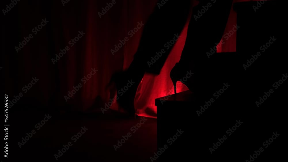 silhouette woman close-up legs walking up the stairs on red background of link. Climb the career ladder concept. Woman go up stairs on the stage in theatre or club. Actress go up stairs on stage.
