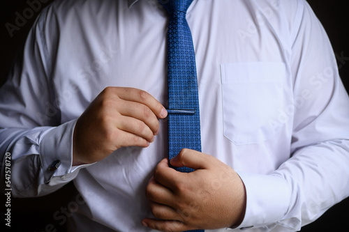 A man in a white shirt puts on and straightens his tie and clip. Wedding day concept, young modern businessman.