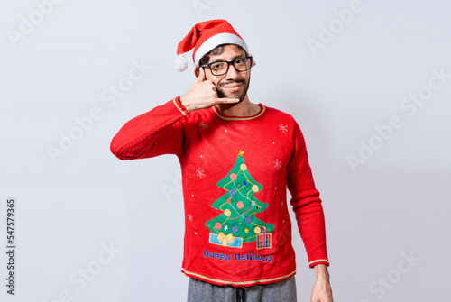 People in Christmas clothes making a call gesture with their fingers. Man in christmas hat imitating a phone conversation, Young latin man in christmas hat making a call gesture isolated