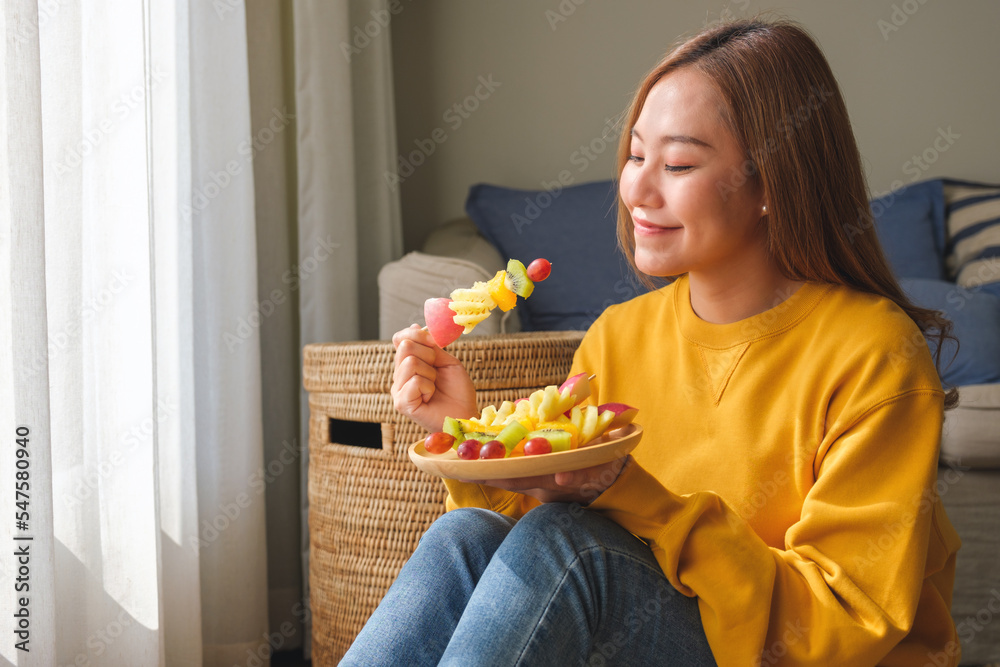 Portrait image of a young woman holding and eating a fresh mixed fruits on skewers Portrait image of a young woman holding and eating a fresh mixed fruits on skewers