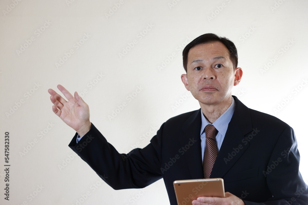 Middle-aged Japanese male businessman wearing navy blue suit on white background holding tablet PC. Conceptual image of a project proposal, strategic business success and negotiation closing. Middle-aged Japanese male businessman wearing navy blue suit on white background holding tablet PC. Conceptual image of a project proposal, strategic business success and negotiation closing.