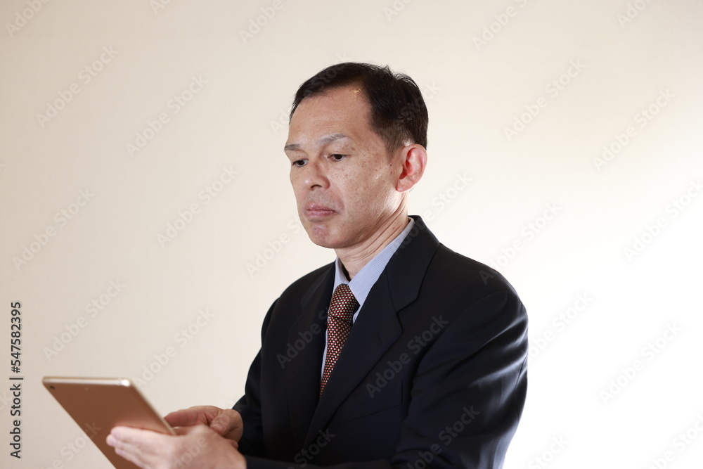 Middle-aged Japanese male businessman wearing navy blue suit on white background holding tablet PC. Conceptual image of a project proposal, strategic business success and negotiation closing. Middle-aged Japanese male businessman wearing navy blue suit on white background holding tablet PC. Conceptual image of a project proposal, strategic business success and negotiation closing.