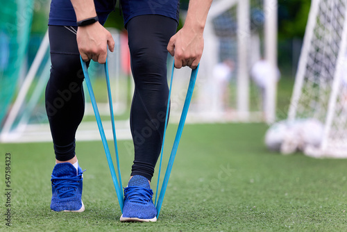 Close-up of the athlete's strong hands pulling an elastic band at a street workout at the stadium. A professional athlete trains at the stadium on an artificial green surface using an elastic band