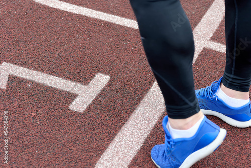 Close-up of the foot of an athlete in blue sneakers kneading his feet before a race on track number one. Runner prepares for a marathon race in the track, number one