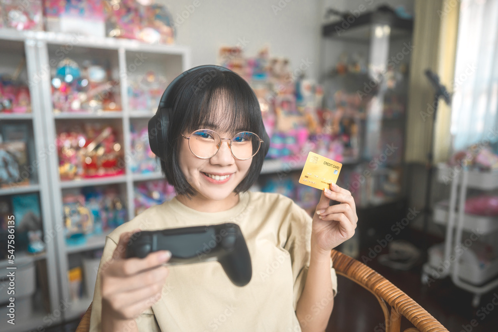 Nerd style young adult asian gamer woman wear eyeglasses and headphone using credit card Nerd style young adult asian gamer woman wear eyeglasses and headphone using credit card
