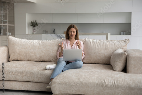 Attractive woman makes video call, talks to friend or by business sit on sofa with laptop. Virtual meeting with family, easy comfort method for communication using modern tech and internet connection