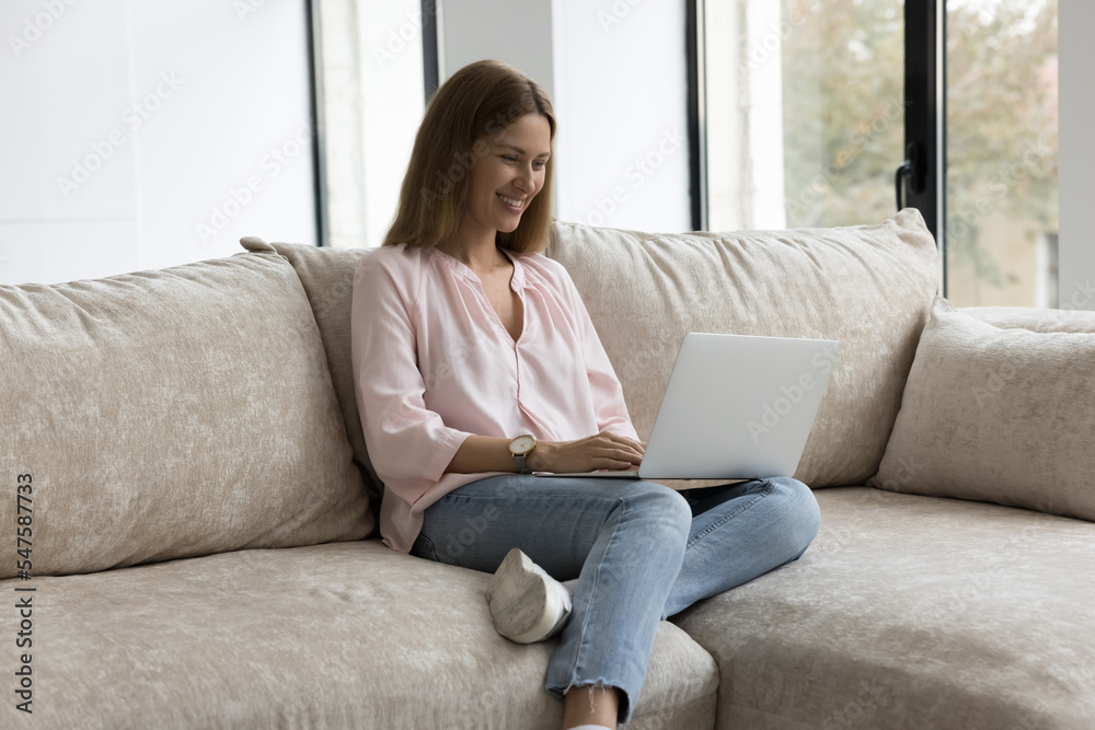 Smiling millennial woman relax on couch use modern laptop, browsing internet feels happy spend leisure online. Female freelancer work on computer typing message, communicates from home use technology Smiling millennial woman relax on couch use modern laptop, browsing internet feels happy spend leisure online. Female freelancer work on computer typing message, communicates from home use technology