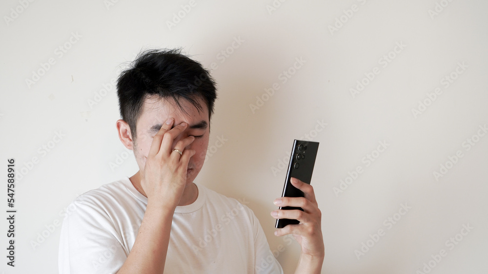 a man is expressing upset and distressed after receiving and reading a bad massage or information shown on a phone he was holding over a white background a man is expressing upset and distressed after receiving and reading a bad massage or information shown on a phone he was holding over a white background