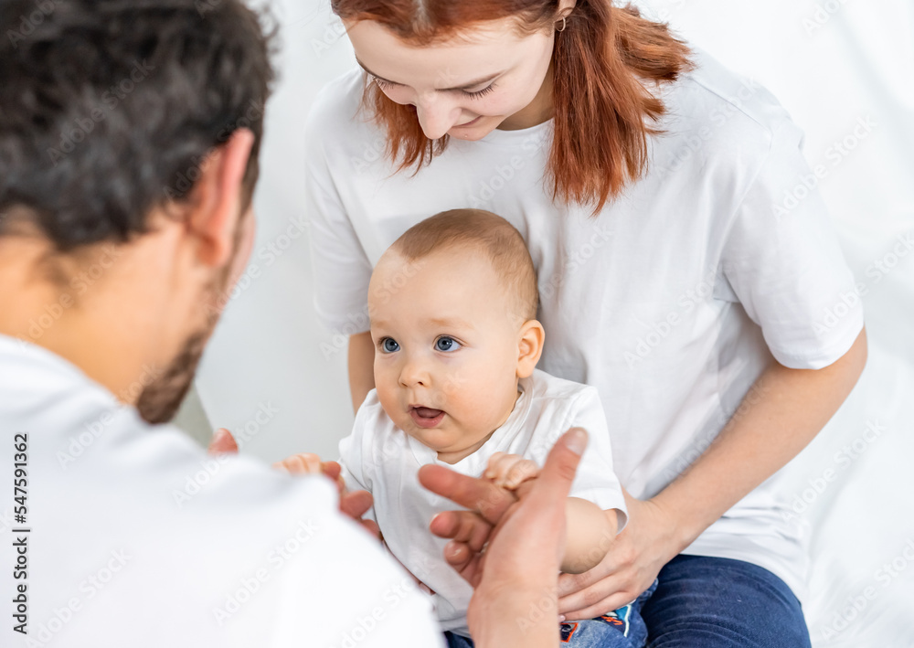 dad and mom play with their son. a child in a white t-shirt and blue jeans crawls on the floor. family in studio or at home dad and mom play with their son. a child in a white t-shirt and blue jeans crawls on the floor. family in studio or at home