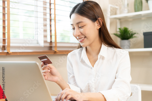 Internet banking, Online shopping at home, happy asian young woman, girl hand in holding credit card, using laptop computer, spending money with purchase, pay on store at home. Shopaholic ecommerce. © KMPZZZ