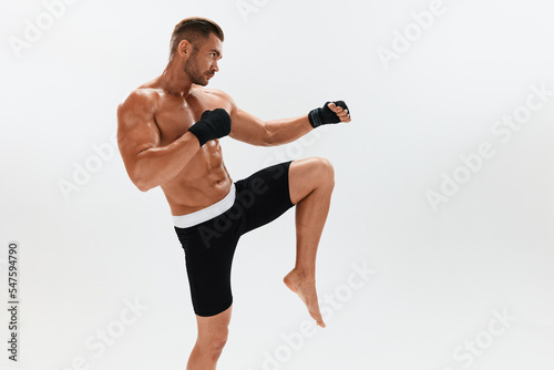 Man athletic bodybuilder poses in boxing gloves with nude torso abs in full-length background, boxing and martial arts. Advertising, sports, active lifestyle, light, competition, challenge concept. 