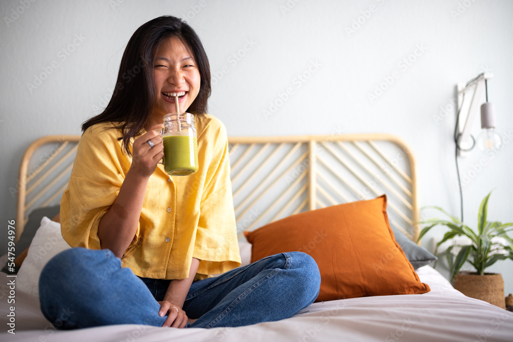 Happy young asian woman laughing. Female Chinese teenager looking at camera drinking green juice smiling. Copy space. Happy young asian woman laughing. Female Chinese teenager looking at camera drinking green juice smiling. Copy space.