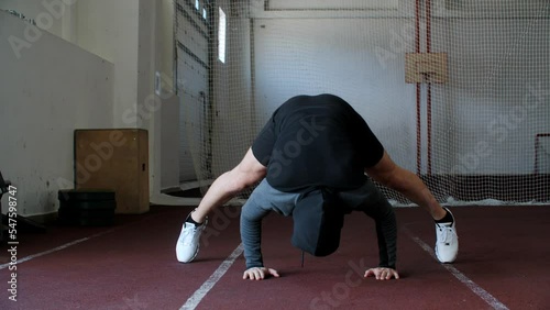 Full length of athletic man doing handstand while exercising in gym. Sportsman is performing balancing exercise at healthcare center. He is wearing hooded shirt during training. Hoody sportsware photo