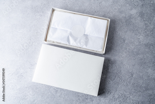 White square gift boxes with tissue wraping paper and round label, mockup on gray concrete background. From above, top view, minimalist concept