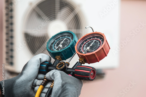 Mechanic air conditioner technician using manifold gauge checking refrigerant for filling home air conditioning and air duct cleaning and maintenance outdoor condition compressor unit.