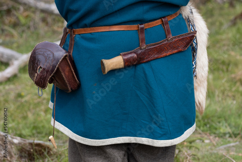 Back view of a viking man in blue wool tunic with sax knife in a  leather sheath and a small leather  bag on the belt. photo
