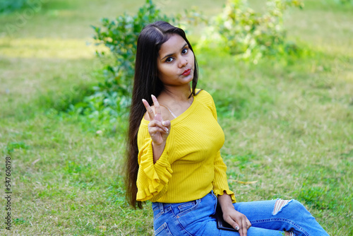 Indian cute student sitting in the park and showing victory symbol