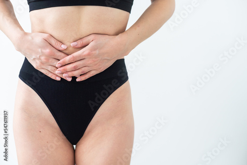 A woman in underwear holds her hands to her lower abdomen. Close-up. Beige background. The concept of gynecology and women's health