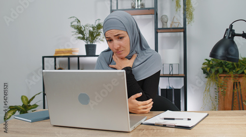 Business woman in hijab thinking about an important creative project work decision at home office desk. Confident muslim freelancer girl busy occupation looking through analytical reports on laptop
