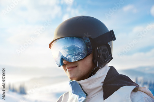 Close Up Of The Ski Goggles Of A Man With The Reflection Of Snowed Mountains. Snowboarder Man on The Background Blue Sky.  Winter Sports