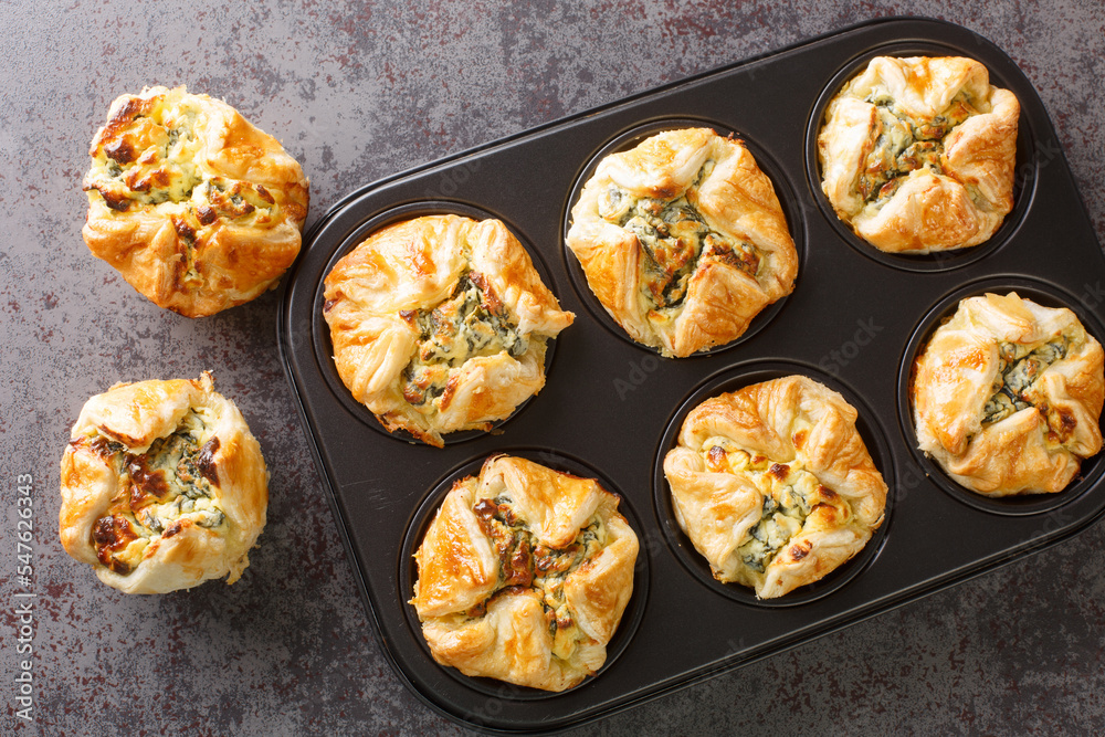 Tasty Spinach Cups Puff with Feta and Onion closeup in the maffin pan on the table. Horizontal top view from above Tasty Spinach Cups Puff with Feta and Onion closeup in the maffin pan on the table. Horizontal top view from above