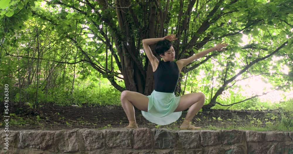 An Asian dancer gets low and bounces to the beat. Wide shot, outdoors in the forest.