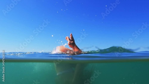 Half underwater scene of young redhead girl rolling back in sea water with horizon in background. Slow motion photo