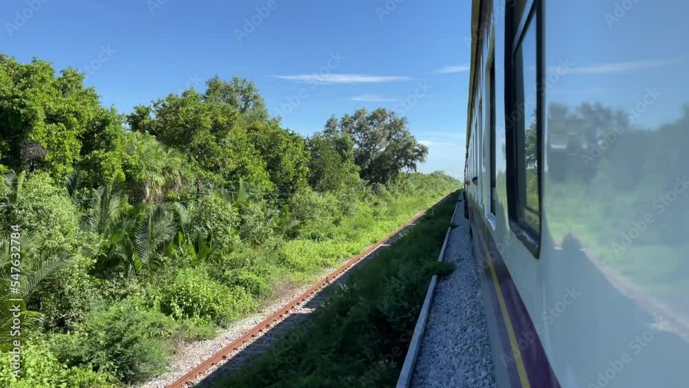 POV view from moving local train on sunny day countryside with nature landscape, trees, train track and blue sky.