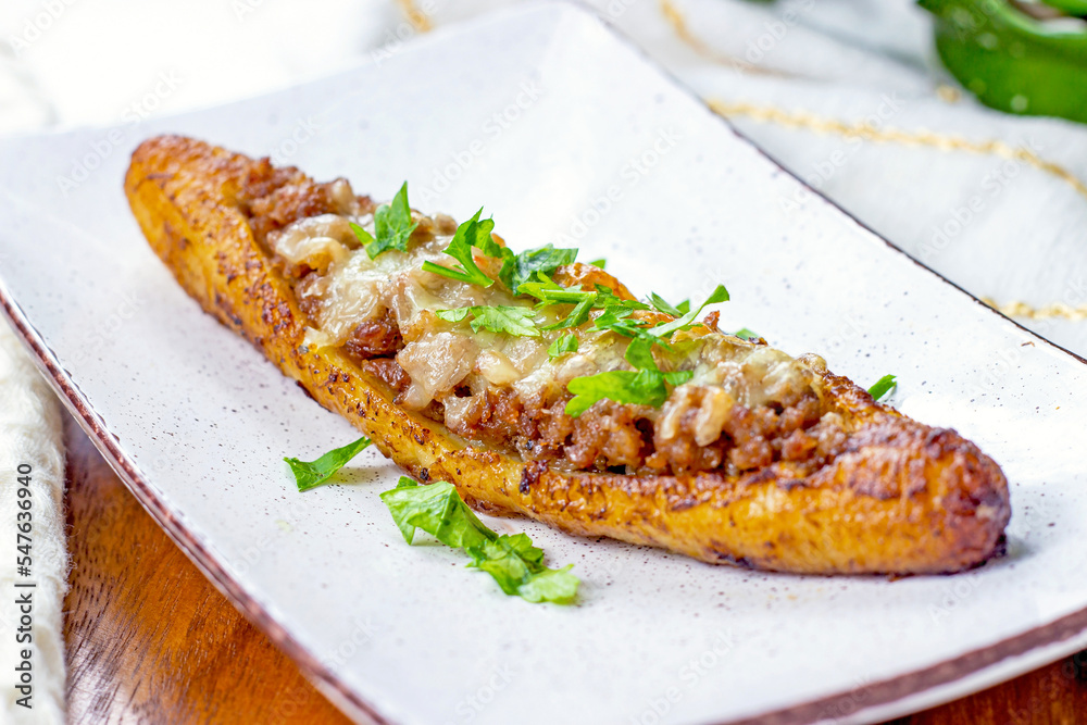 Baked Sweet Ripe Plantain Canoe (Canoas de Platanos Maduros) stuffed with ground meat, cheese and greens on a plate on wooden background. Baked Sweet Ripe Plantain Canoe (Canoas de Platanos Maduros) stuffed with ground meat, cheese and greens on a plate on wooden background.