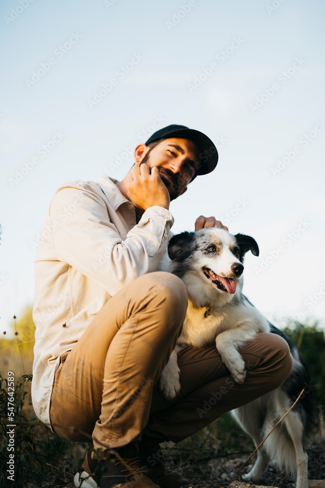 Portrait of a young bearded man wearing a black cap, with his dog, at countryside Portrait of a young bearded man wearing a black cap, with his dog, at countryside