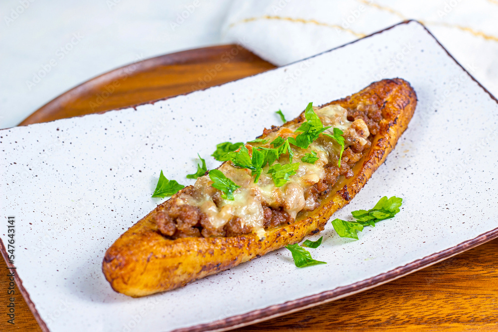 Baked Sweet Ripe Plantain Canoe (Canoas de Platanos Maduros) stuffed with ground meat, cheese and greens on a plate on wooden background. Baked Sweet Ripe Plantain Canoe (Canoas de Platanos Maduros) stuffed with ground meat, cheese and greens on a plate on wooden background.