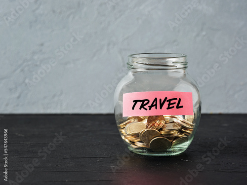 Glass jar with coins and the word travel on a label. Saving money for holiday travel and budget for vacation.