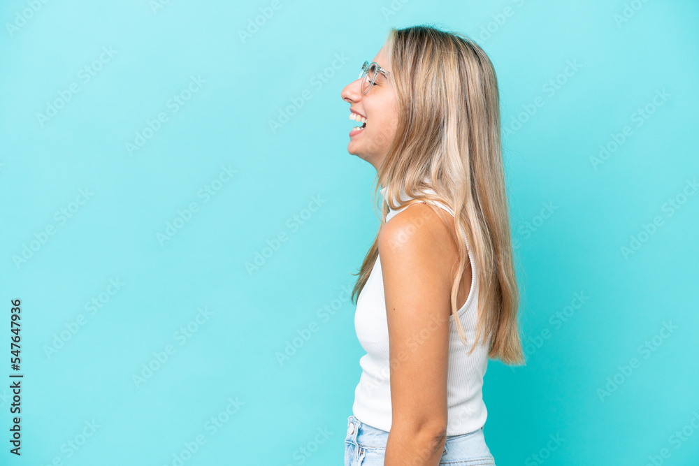 Naklejka premium Young caucasian woman isolated on blue background laughing in lateral position