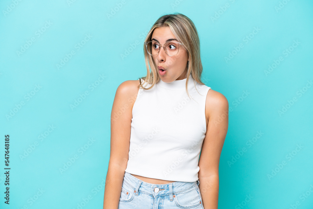 Young caucasian woman isolated on blue background doing surprise gesture while looking to the side Young caucasian woman isolated on blue background doing surprise gesture while looking to the side