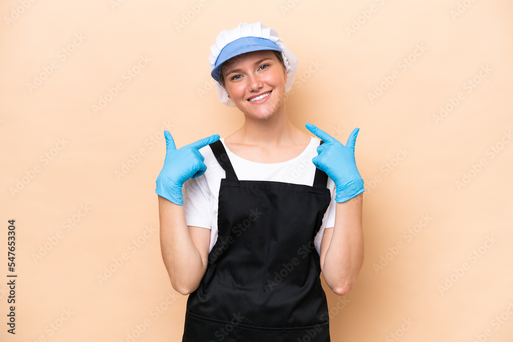 Fishmonger caucasian woman wearing an apron and holding a raw fish isolated on beige background giving a thumbs up gesture Fishmonger caucasian woman wearing an apron and holding a raw fish isolated on beige background giving a thumbs up gesture