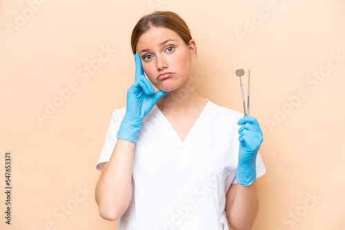 Dentist caucasian woman holding tools isolated on beige background thinking an idea