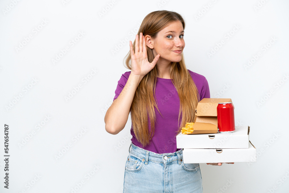 Young pretty blonde woman holding fast food isolated on white background listening to something by putting hand on the ear Young pretty blonde woman holding fast food isolated on white background listening to something by putting hand on the ear