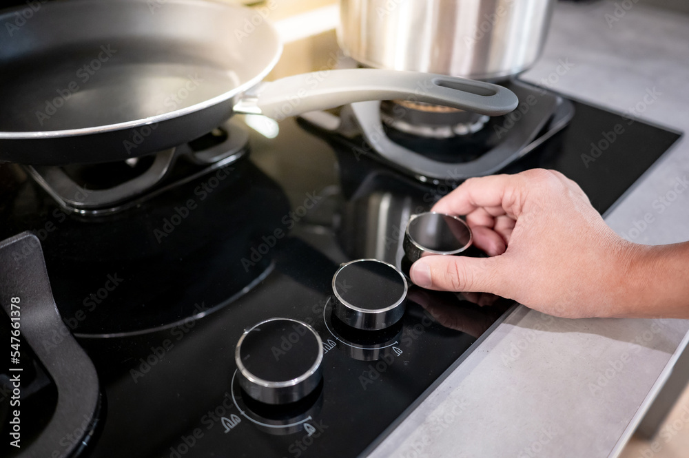 Male hand turning switch knob on modern gas stove in kitchen showroom. Cooking appliance in domestic kitchen. Home improvement and House interior design concepts Male hand turning switch knob on modern gas stove in kitchen showroom. Cooking appliance in domestic kitchen. Home improvement and House interior design concepts