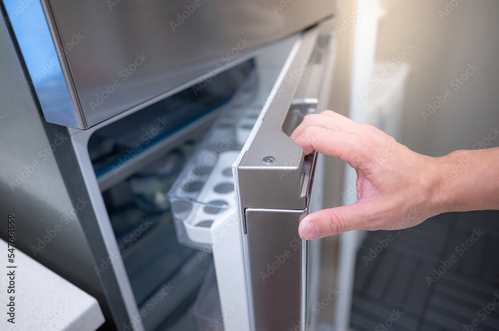 Male hand opening fridge or refrigerator door in kitchen showroom. Buying appliance for home interior design. Male hand opening fridge or refrigerator door in kitchen showroom. Buying appliance for home interior design.