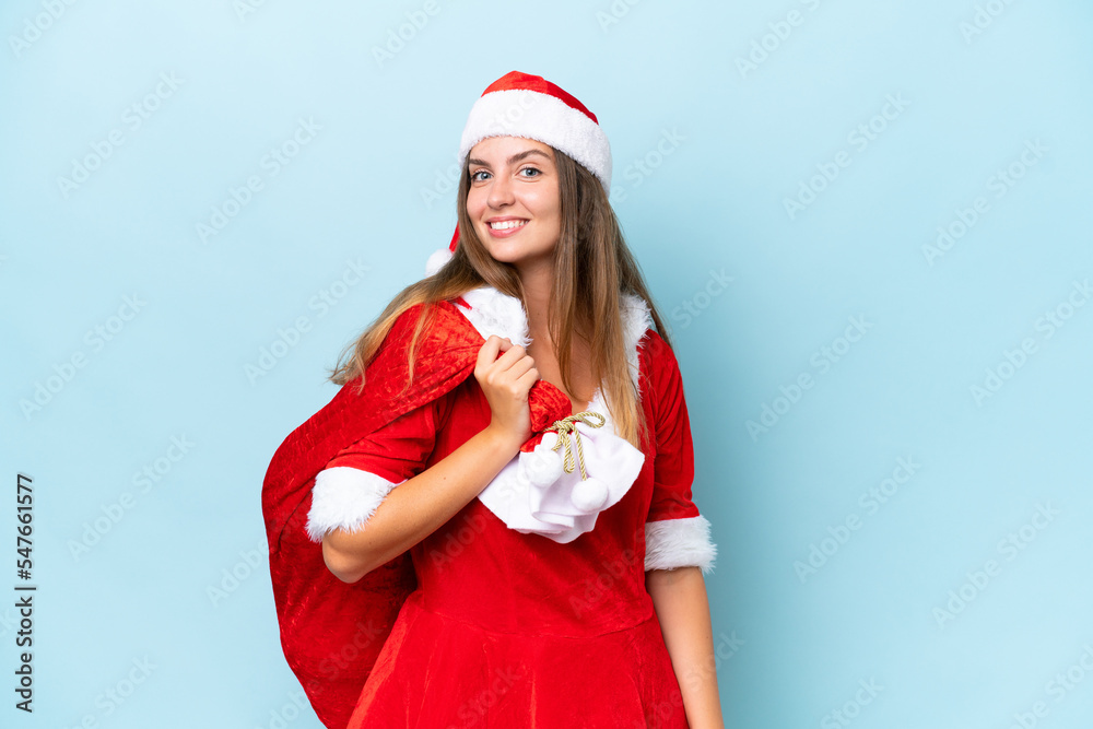 Young caucasian woman dressed as mama noel holding Christmas sack isolated on blue background smiling a lot Young caucasian woman dressed as mama noel holding Christmas sack isolated on blue background smiling a lot